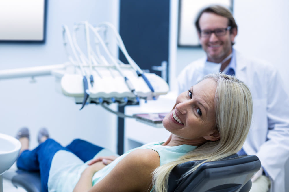 Dentista no consultório e sua paciente na cadeia de odontologia com expressão felizes por resolver suas dores no maxilar. Solumedi agendamentos e de consultas e exames saúde São José dos campos SJC