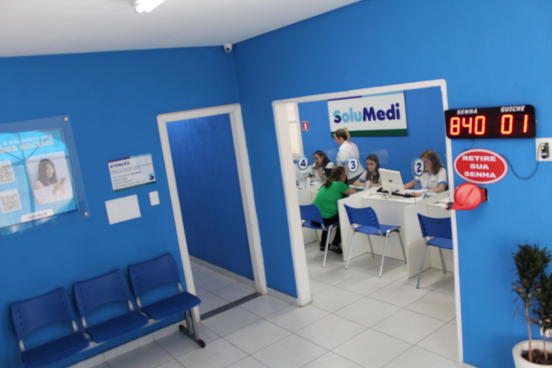 Imagem real da unidade Solumedi agendamentos e de consultas e exames saúde São José dos campos SJC. sala de espera com cadeiras, ambiente de agua e cafezinho enquanto espera sua vês na chamada pela senha no painel digital. Solumedi agendamentos e de consultas e exames saúde São José dos campos SJC